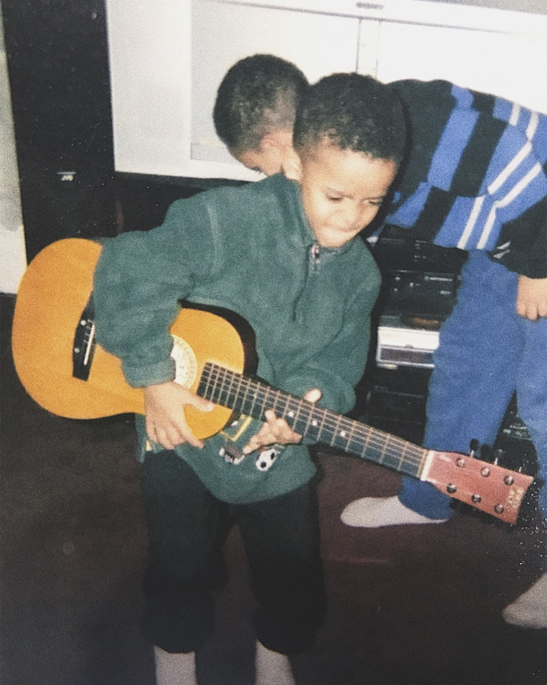 Archival childhood photograph of Brandon Miles playing an acoustic guitar