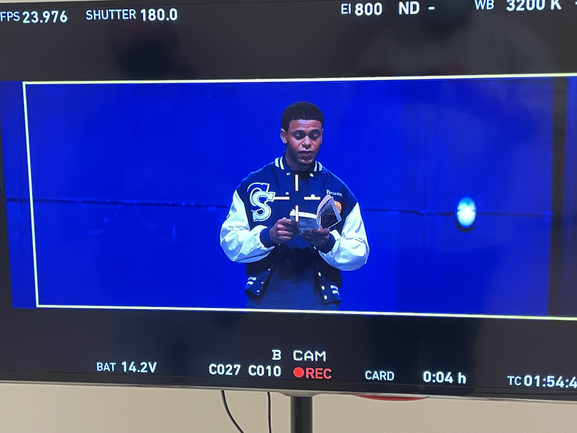 An on-set production monitor showing Brandon Miles performing in a blue-lit scene